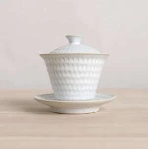 Full view of textured white ceramic gaiwan with gold trim on saucer